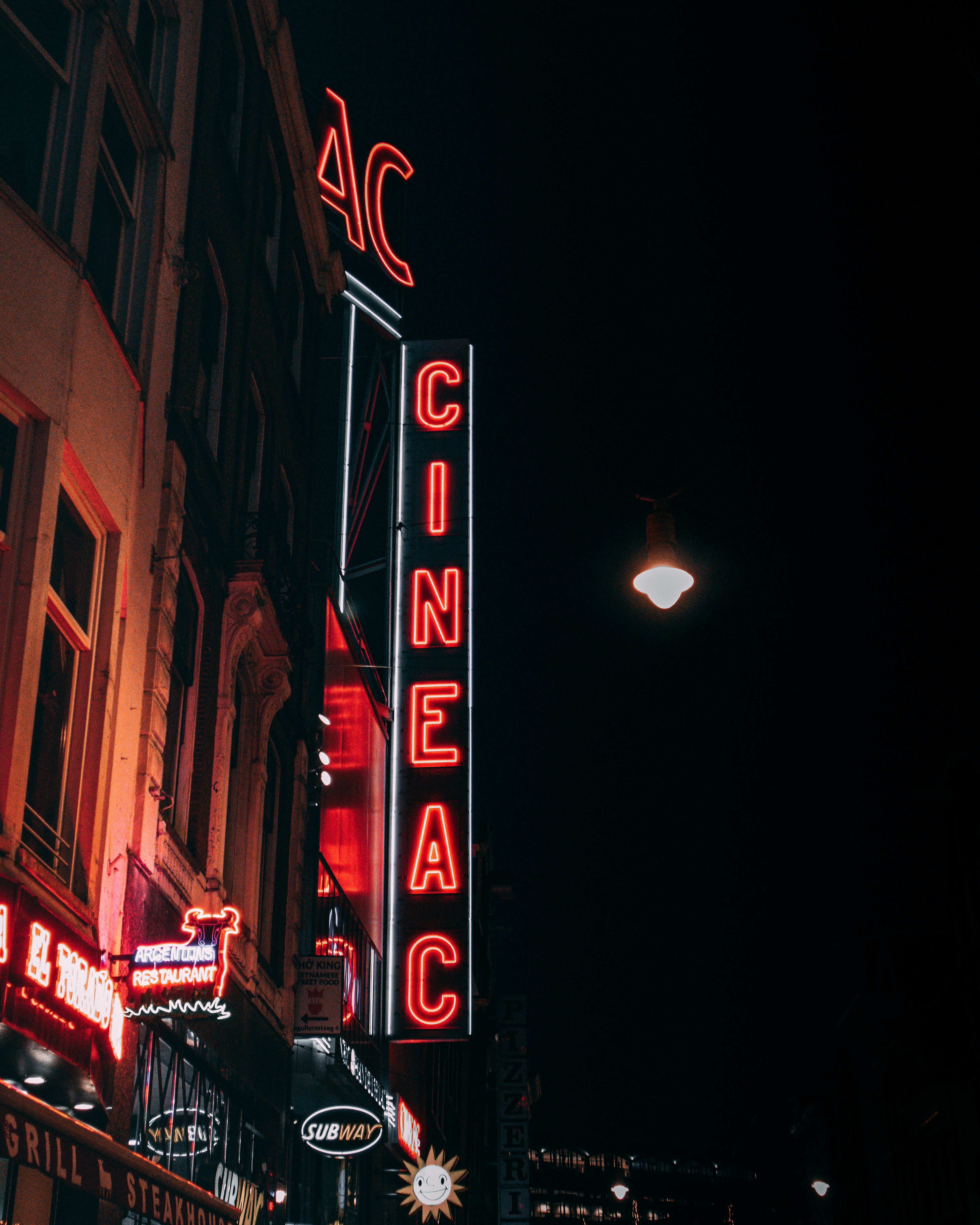 Red neon cinema sign glowing on a city street at night